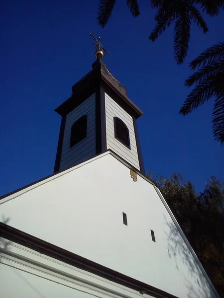 Roof and church dome with a cross. Christian temple, plastered and painted white. The sound of a small wind window and a belfry with a bell. Gilded cross against a blue sky