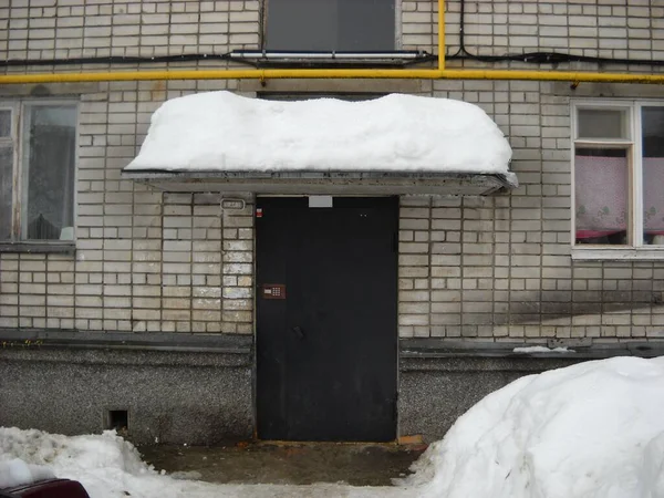 Snow blockages near the entrance of an apartment building. Poor work of housing and communal services. Metal door with intercom. Brick walls and a dirty porch cleaned from snow. Snow on the visor — Stock Image Snow blockages near the entrance of an apartment building. Poor work of housing and communal services. Metal door with intercom. Brick walls and a dirty porch cleaned from snow. Snow on the visor Stock Picture