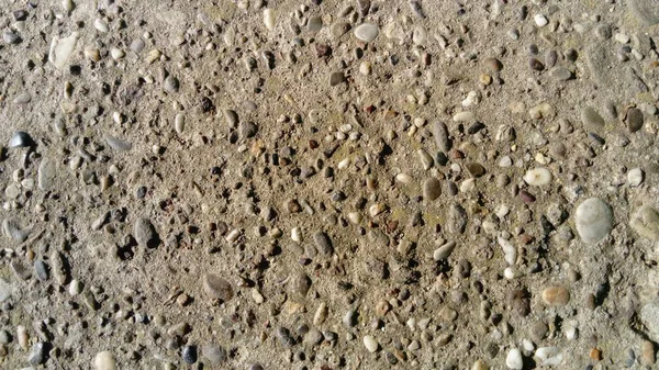 Destroyed concrete pavement. Small stones of different colors come out. A play of light and shadow on an uneven surface is created. Ground with dust and sand mixed. Close-up — Stock Photo, Image