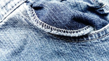 Biraz bükülmüş bir kot pantolon cebi. Mavi paçoz kot. Cebin kenarına kapalı bir makine dikilmiş durumda. Beyaz renkli pamuk iplikleri.