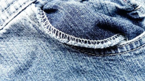 Una tasca leggermente contorta in jeans. Denim blu squallido. Una cucitura a macchina nuvolosa intorno al bordo dell'interno della tasca. Filati di cotone di colore bianco . — Foto Stock