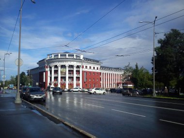 Yağmurdan sonra şehrin merkez caddesi. Yollarda ıslak asfaltlar. Güzel balkonları ve terasları olan bir otel binasının kırmızı ve beyaz cephesi.