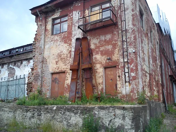 Huge skis near the facade of the factory floor. Skis and ski poles are made of rusting metal and lean against the wall. Abandoned tractor factory. Oxidation of iron. The shabby facade of the building — Stock Photo, Image