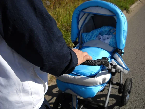 Un hombre lleva un cochecito azul con un bebé dentro. Cumplimiento del régimen. Paseo diurno de verano en clima fresco —  Fotos de Stock
