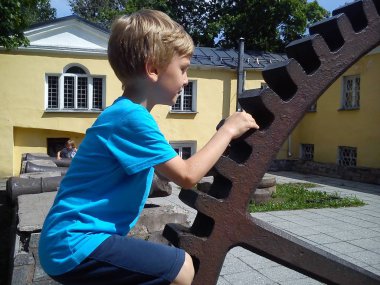 Çocuklar eski bir top fabrikasının kalıntıları üzerinde yürüyorlar. Sarı saçlı, mavi tişörtlü bir çocuk dökme demir fabrikasının dişlerine elleriyle tırmanıyor. Teçhizat saat gibi çalışıyor. Eski bina