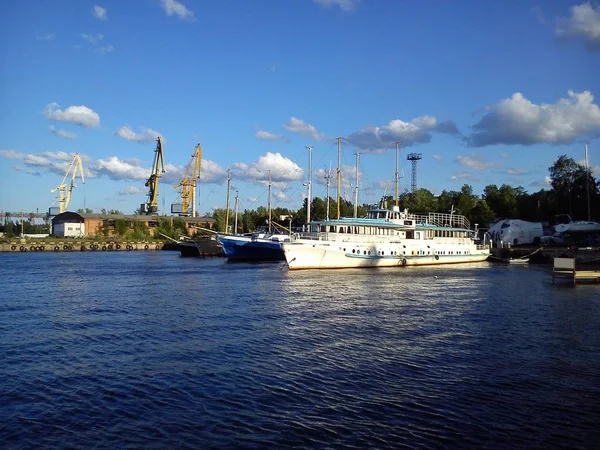 Les bateaux sont dans le port. Beau temps, calme. Ciel bleu avec nuages. Plusieurs grues sur une colline. Un bateau de plaisance blanc est éclairé par le soleil du soir. Navire maritime se reflète dans l'eau — Photo