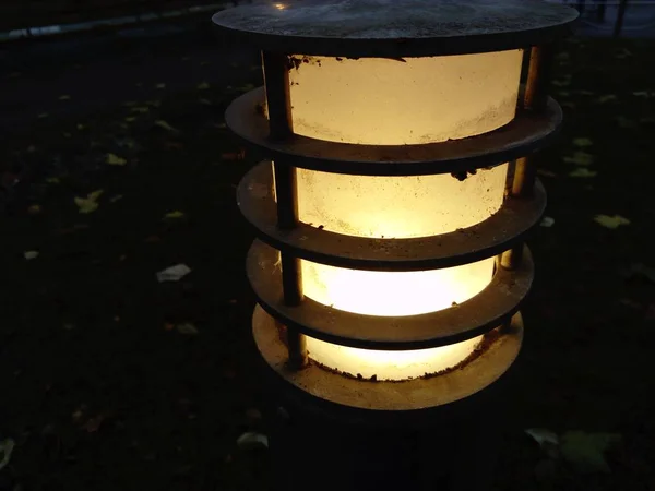 Farola en un parque de la ciudad. Vidrio esmerilado con luz amarilla cálida esmerilada. Llanta metálica o jaula en la que se coloca una bombilla de vidrio. Luz amarilla en la noche oscura — Foto de Stock