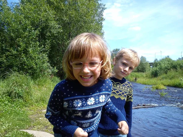 Erkek ve kız kardeş nehrin yanında yürüyorlar. Oğlan ve kız mavi kot pantolon ve mavi örülmüş kalın kazaklar ve yeni yıl süslemeleri giyiyorlar. Yazın başında. Konuşma ve oyun