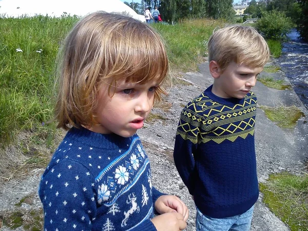 Erkek ve kız kardeş nehrin yanında yürüyorlar. Oğlan ve kız mavi kot pantolon ve mavi örülmüş kalın kazaklar ve yeni yıl süslemeleri giyiyorlar. Yazın başında. Konuşma ve oyun