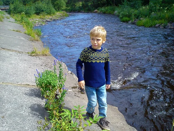 Bruder und Schwester spazieren in der Nähe des Flusses. Der Junge und das Mädchen sind mit blauen Jeans und blauen Strickpullovern und Pullovern mit Neujahrsschmuck bekleidet. Frühsommer. Unterhaltung und Spiel — Stockfoto