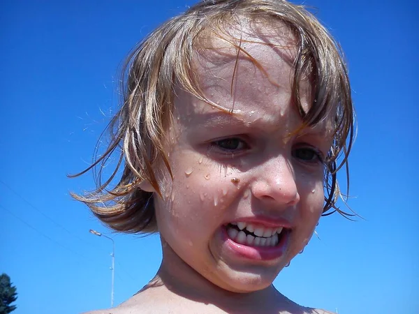 Bebé mojado después de nadar en el mar. Retrato de una chica. Cabello y cara húmedos. Una mueca en la cara del niño. Cielo azul y arena amarilla. Descansa en el resort. Gotas de agua en la piel hermosa . —  Fotos de Stock