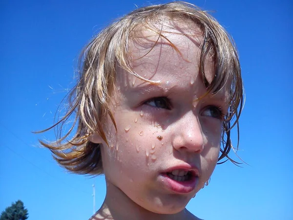 Blöt barnet efter att ha badat i havet. Porträtt av en flicka. Vått hår och ansikte. En grimace i ansiktet på barnet. Blå himmel och gul sand. Vila på anläggningen. Droppar vatten på vacker hud. — Stockfoto