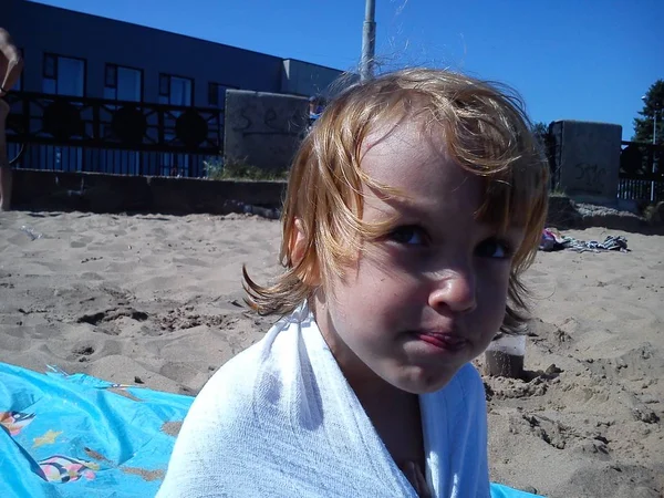 Bebê molhado depois de nadar no mar. Retrato de uma rapariga. Cabelo molhado e rosto. Uma careta no rosto da criança. Céu azul e areia amarela. Descanse no resort. Gotas de água na bela pele . — Fotografia de Stock