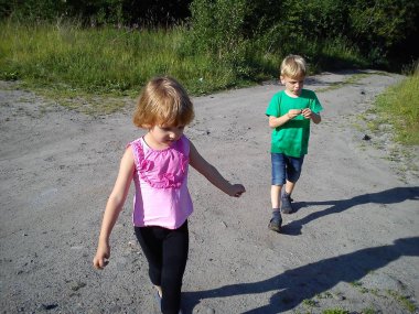 Sarışın çocuklar yazın toprak bir yolda yürürler. - Öyle mi? Yeşil tişörtlü çocuk. Pembe bluzlu fırfırlı bir kız. Erkek ve kız kardeş eve koştu. Güneşli havada doğa yürüyüşü. Süpürme hareketleri.