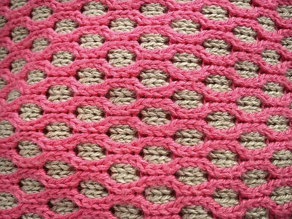 Close-up of decorative knitting. Machine or neat hand-knitted thing. The basis is beige yarn, the outer ornament is pink threads of the same thickness. Smooth hinges. Ovals or honeycombs as a pattern. — 스톡 사진