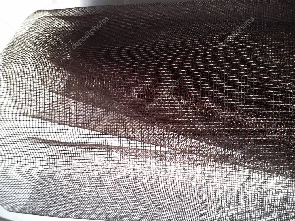 Mosquito net in a roll. Brown synthetic material on a white background. Weaving plastic threads. Convoluted lattice.