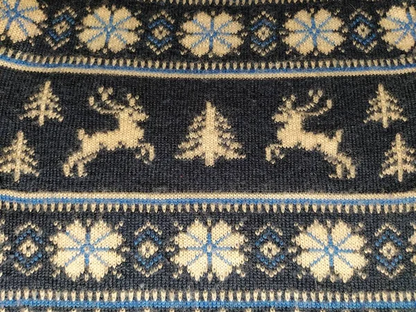 A fragment of an ornament on a knitted polyester or woolen sweater. Winter motives. Blue threads for hand knitting. White thread knitted pattern. Flowers and deer — Stock Photo, Image