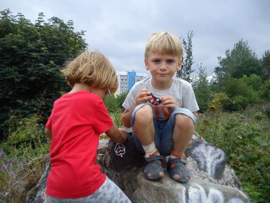 Bir erkek ve bir kız kardeştir. Sarı saçlı çocuklar ağaçların ve çalıların yanında yürürler. Gözlüklü ve kırmızı tişörtlü kız. Çocuklar büyük bir kaldırıma tırmandılar - parke taşı. Dalgın yüzler