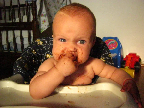 Малюк їсть шоколадний кекс і смішно похмуро. Дитині 1 рік. Дитина сидить на кріслі — стокове фото