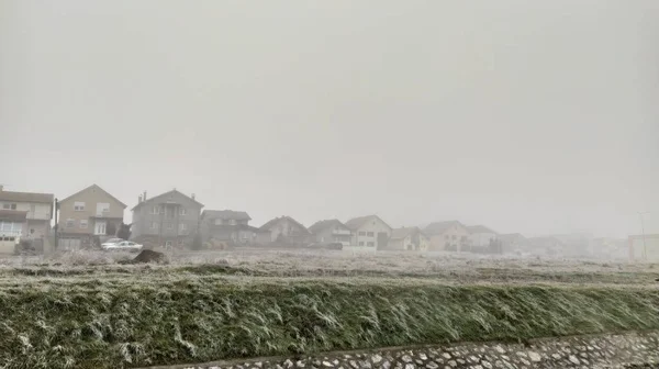 Téli hideg ködös nap. Panoráma. Magas páratartalom. Mező fagyott jeges fűvel. Messze, otthon, egy ködös szürke ködben. Senki sincs az utcán. Nyugodtság, homály, csend és melankólia. — Stock Fotó