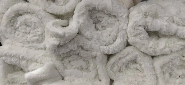 Soft fluffy white rugs folded into skeins, rolles and bundles. An assortment of light bedspreads on a store shelf. The blankets are beautifully laid out for sale. White synthetic fleecy fabric — Stock Photo, Image