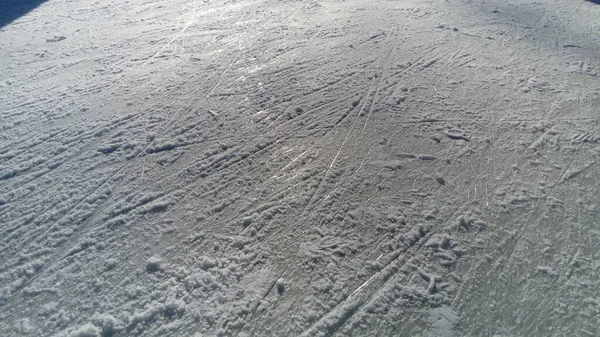Ghiaccio striato con la punta dei pattini. Pattinaggio artistico sul ghiaccio. La superficie della pista di pattinaggio dopo l'esercizio pattinatori. Raggio di sole sul ghiaccio di sorgente bagnato. Neve e acqua ghiacciata — Foto Stock