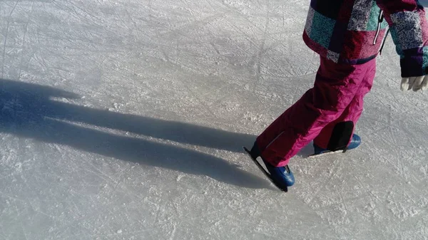 I bambini viaggiano in un parco cittadino su una pista di pattinaggio. Gambe e mani di un pattinatore mentre pattina sul ghiaccio. La ragazza è vestita in abbigliamento sportivo rosa. Pattini di figura blu vestiti su gambe . — Foto Stock