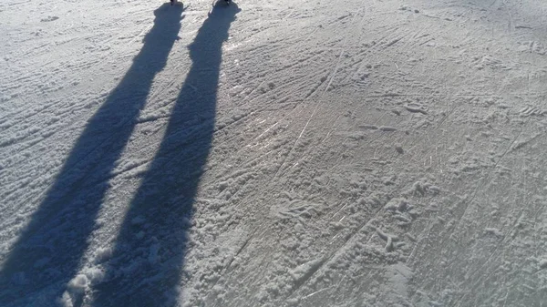 As crianças andam em um parque da cidade em uma pista de gelo. Pés patinador enquanto patina no gelo. O sol baixo do inverno ilumina fracamente o gelo. Formas escuras e longas sombras na superfície. Movimentos desportivos — Fotografia de Stock
