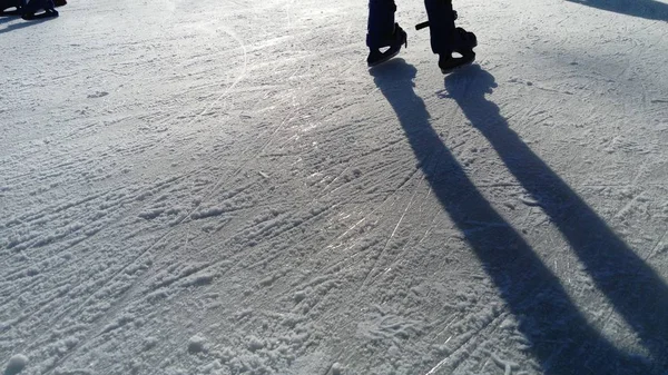 Children ride in a city park on an ice rink. Feet skater while skating on ice. The low winter sun weakly illuminates the ice. Dark shapes and long shadows on the surface. Sports movements — 스톡 사진