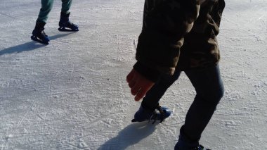 Çocuklar buz pistindeki bir şehir parkında ata biniyorlar. Buz üstünde kayarken bir patencinin elleri ve bacakları. Bacakları üzerinde artistik patenler. Kış güneşinin uzun gölgeleri