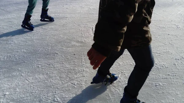 Barn rider i en stadspark vid rinken. Ben och händer av en skridskoåkare medan skridskoåkning på is. Konståkare klädda på ben. Långa skuggor från den låga vintersolen — Stockfoto