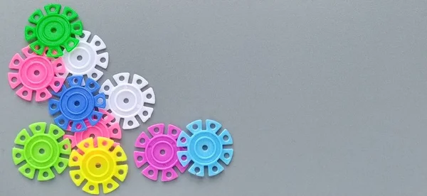 Multi-colored details in the form of snowflakes from the childrens designer on a gray background.Red, yellow, green, blue, white, pink plastic discs for the development of fine motor skills of fingers — Stock Photo, Image