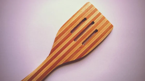 Wooden spatula for gentle cleaning of food that has dried up on dishes or burned to a pan. New wood tool with slots and dark stripes. Pink background with light vignetting. — Stock Photo, Image