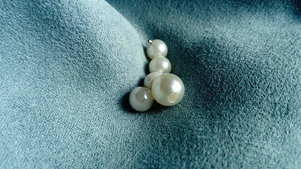 White beads lie on a velvet blue fabric. Jewelry on the curtains. A beautiful combination of mother-of-pearl shine and light tints on a short pile of velvet. Creases and waves on the fabric — Stok fotoğraf