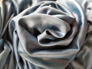 İpeksi, parlak bir ışıltıyla gri-mavi dokuya dokunuyor. Doğal ışıklandırma, ışık ve gölge. Kumaş gelişigüzel bir şekilde bir gül goncasını andıran bir daire şeklinde katlanmış. Polyester Tekstil.