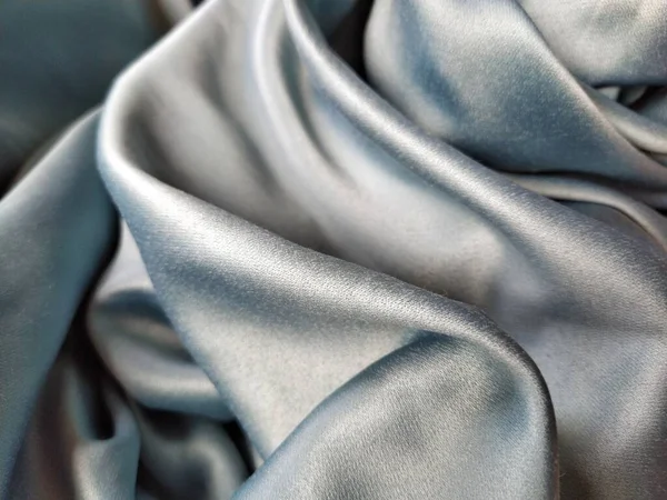 Silky to the touch fabric of gray - blue color with a brilliant shimmer. Natural lighting, light and shadow. The material is casually folded. Polyester Textile.