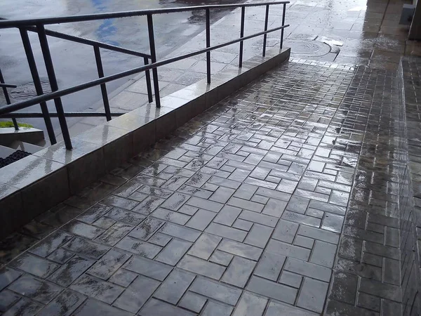 Metalowe poręcze na schodach po deszczu na tle mokrych płyt chodnikowych — Zdjęcie stockowe