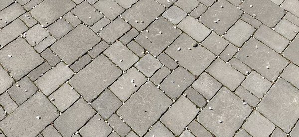 Cobbled street of the old city, lined with square and rectangular stone tiles in a chaotic manner. Soft gray color. The texture of the stone. Geometric pattern