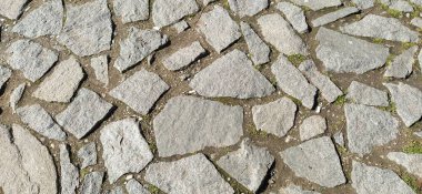 Asfalt düz olmayan gri ve kahverengi taşlarla döşenmiş. Ezilmiş kaldırım taşları arasında küçük çakıl taşları vardır. Toprak, kum, çimen. Güneş ışığı. Eski Avrupa şehrinin meydanında.