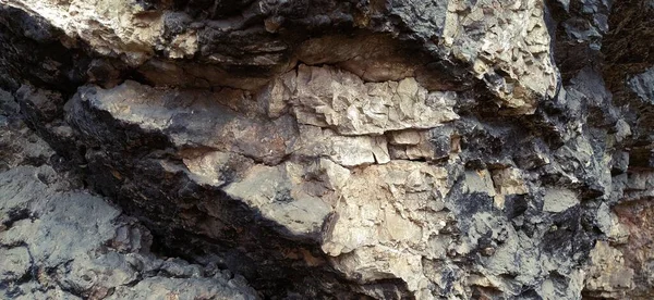 Stone black rock close-up. Ancient frozen lava. Layers and strata of rocks. The texture of dark gray stone. Natural bright gloomy colors