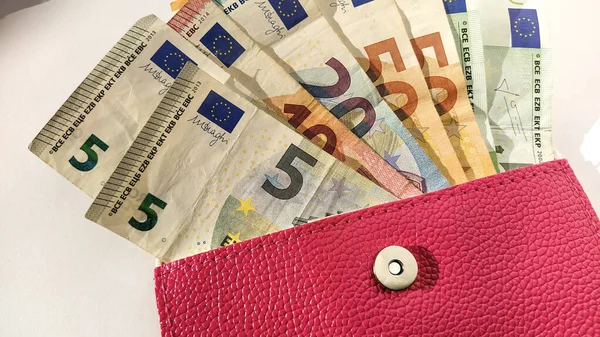 Euro paper notes. European currency on a white background close-up. A purse or purse of bright pink color with a metal button, from which money is spread out. Banknotes of 5, 10, 20, 50 and 100.
