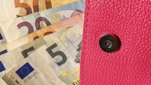 Euro paper notes. European currency on a white background close-up. A purse or purse of bright pink color with a metal button, from which money is spread out. Banknotes of 5, 10, 20, 50 and 100.