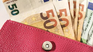 Avro kâğıdı. Beyaz arka planda Avrupa para birimi. Metal düğmeli parlak pembe renkli bir çanta ya da çanta. Paralar oradan yayılıyor. Banknotlar: 5, 10, 20, 50 ve 100.