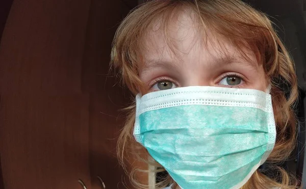 Лицо красивой белой шестилетней девочки в зеленой защитной хирургической маске. Лицо с глазами с серой радужкой. Светлые волосы. Защита от вирусов — стоковое фото