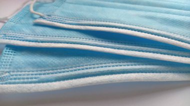 Mavi koruyucu yüz maskesi. Koronavirüs ve bulaşıcı patojenler için ilaç. Sentetik malzeme. Yakın plan. Gündüz ışığı. Beyaz narin arkaplan.