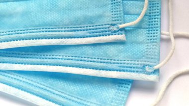 Yüz için mavi renkli üç koruyucu cerrahi maske. Koronavirüs ve bakteriyel bulaşıcı patojenler için ilaç. Sentetik malzeme. Yakın plan. Gündüz ışığı. Beyaz narin arkaplan.