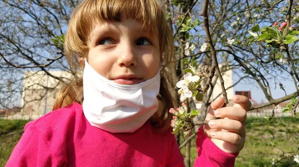 귀여운 소녀가 수술용 보호용 마스크를 사과나무에 아름다운 냄새를 맡는다 병에서 — 스톡 사진