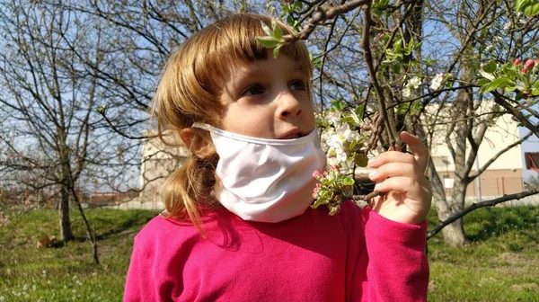 귀여운 소녀가 수술용 보호용 마스크를 사과나무에 아름다운 냄새를 맡는다 병에서 — 스톡 사진