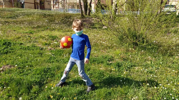 축구공을 수술용 보호용 마스크를 귀여운 잔디에 잔디와서 있습니다 아이는 청바지와 — 스톡 사진