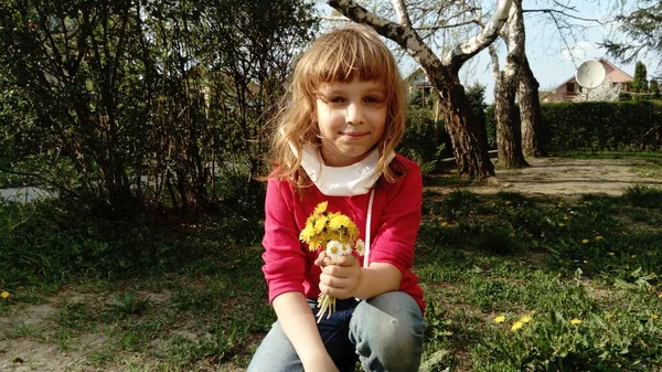 一个6岁的漂亮姑娘 一头金发蜷缩在草坪上 手里拿着一束黄色的野花 白色防护外科口罩从脸上垂下来 过敏原和病毒 — 图库照片